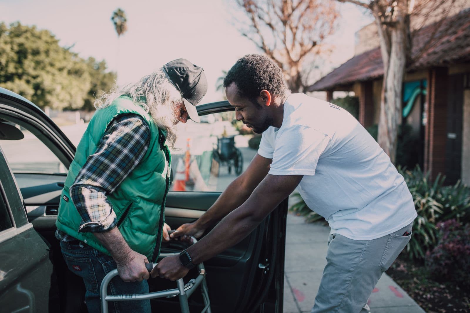 A support worker helping an older man with a walking frame outside his home